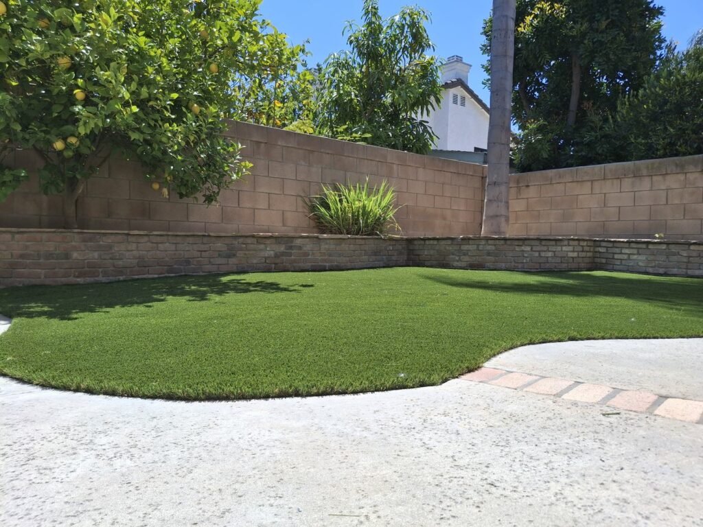 Artificial grass lawn with shade from trees along a block wall