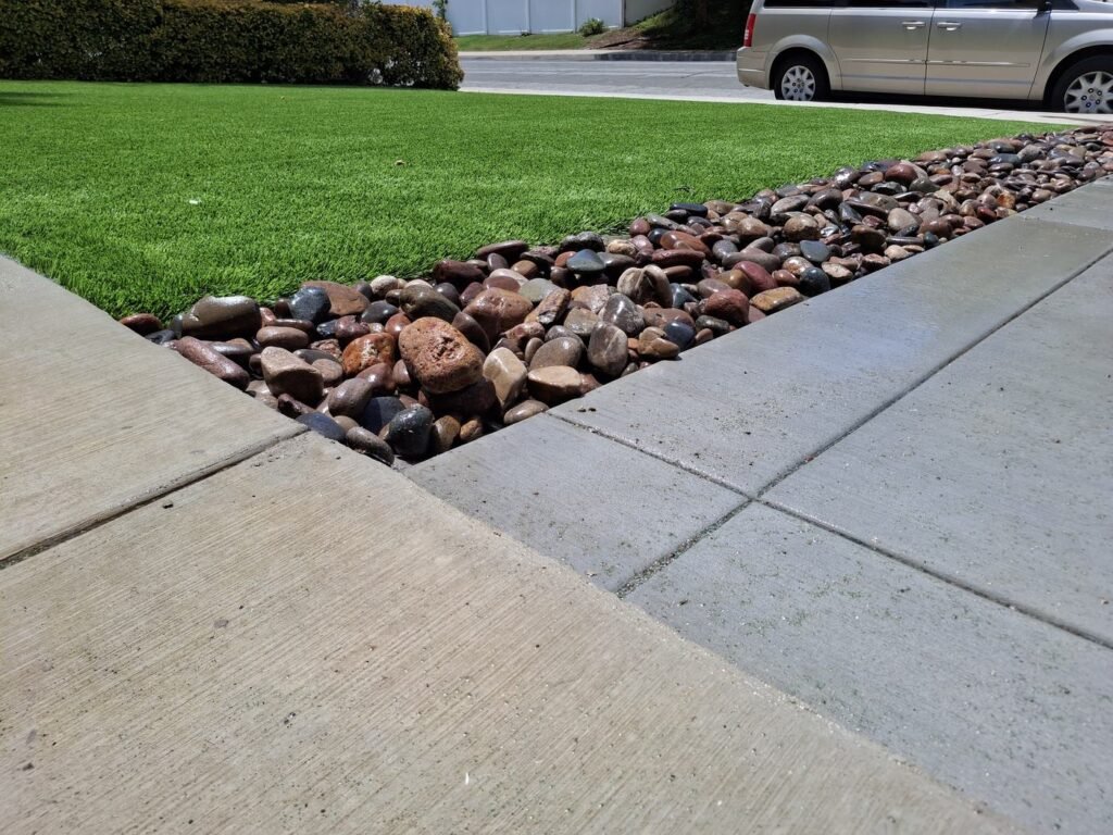 Front lawn artificial grass with a river rock edge along the driveway