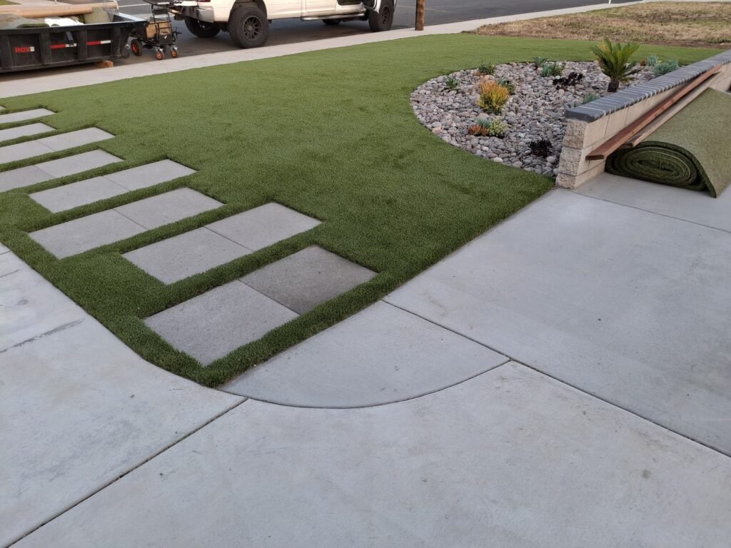 Front yard artificial grass with diagonal stepping pads and a raised planter