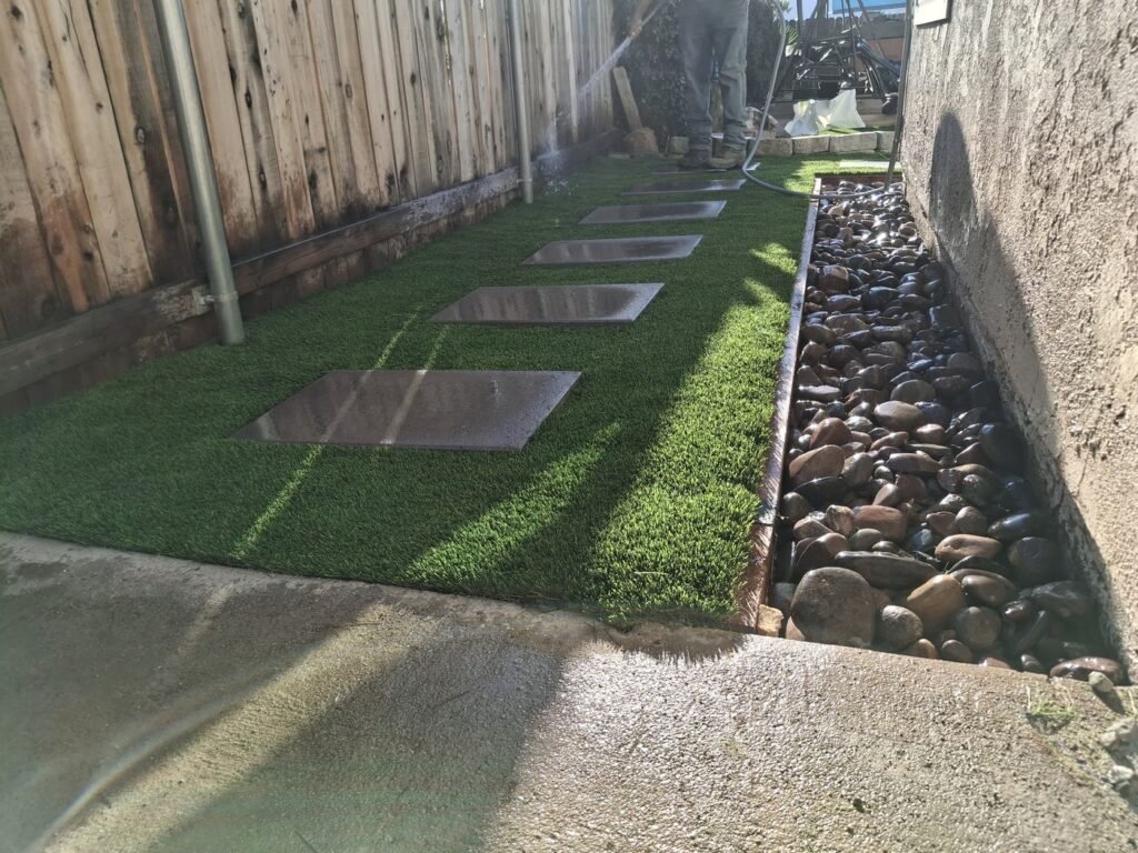 Side yard artificial grass with stepping pads and a rock border