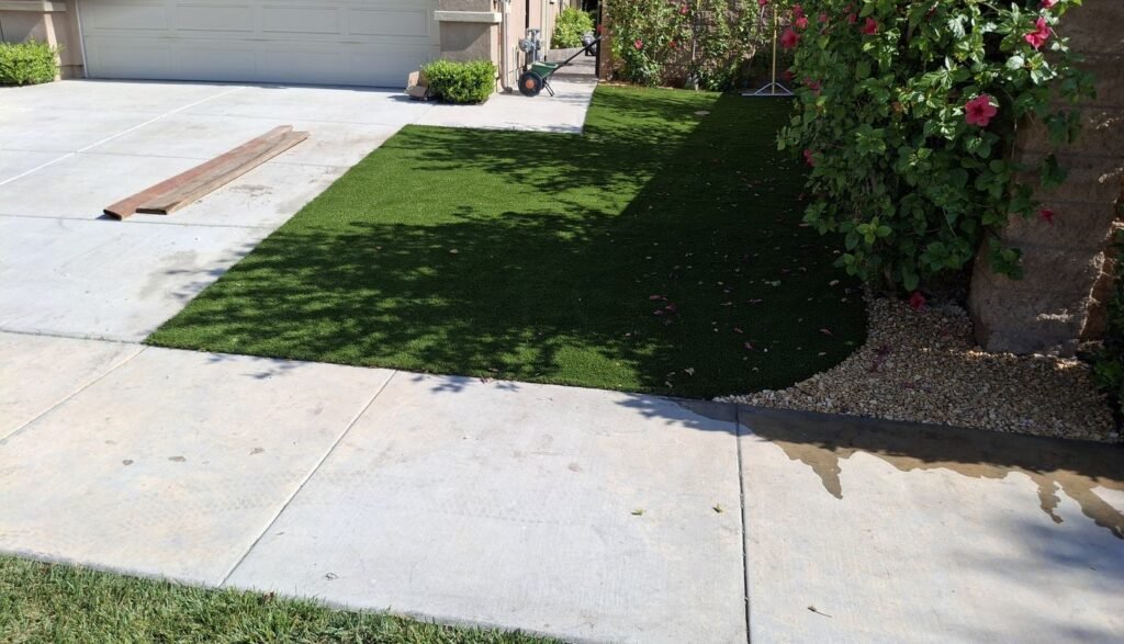 Artificial grass strip beside a driveway with flowering shrubs